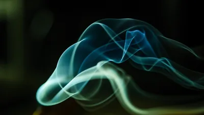 Pale smoke curling through darkness, lit from one side.