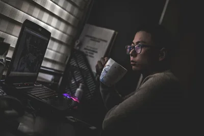 A laptop open on a dark desk, its screen glow lighting the keys.